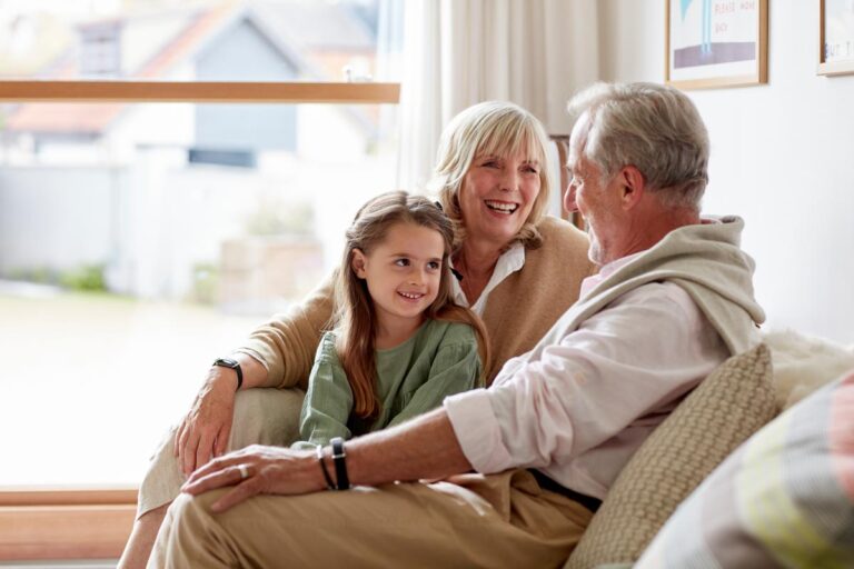 Älteres Ehepaar mit Hilo Band am Arm sitzt mit Enkelkind auf dem Sofa