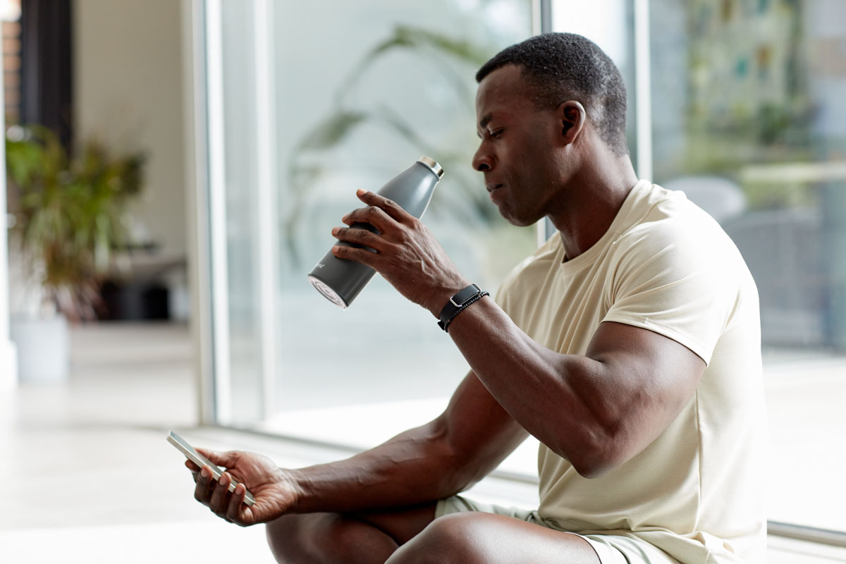 Mann trägt Hilo Band, trinkt aus Wasserflasche und schaut auf Handy
