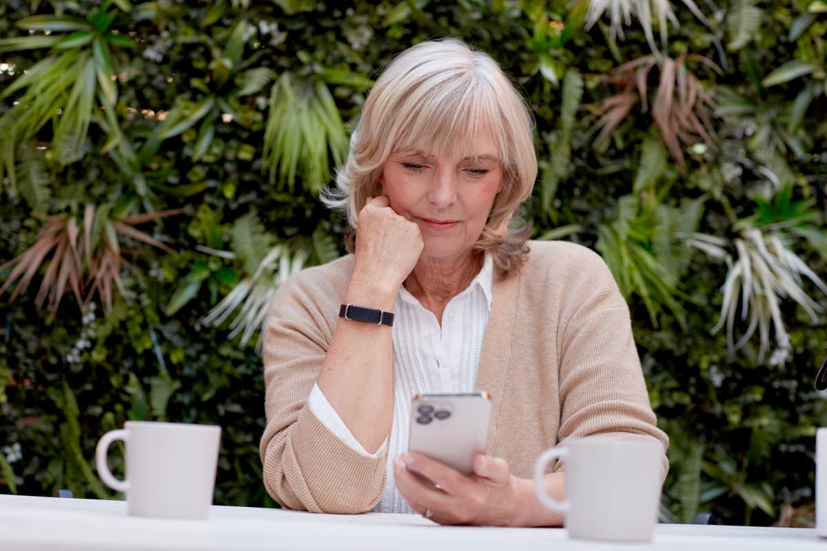Ältere Frau mit Hilo Band schaut aufs Handy
